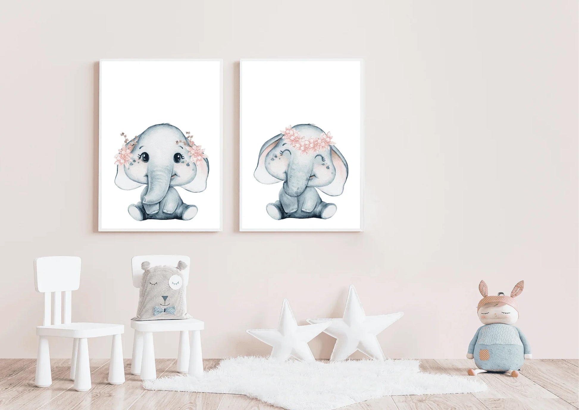 A serene nursery room featuring a white wooden crib draped with a soft, sheer canopy. Above the crib, two matching white-framed watercolor elephant prints are hung side-by-side. The grey elephants wear delicate pink flower crowns. The room includes a round rug, natural light, and a small pink stuffed toy on the crib, showcasing a peaceful celestial animal theme in soft pink and grey tones.