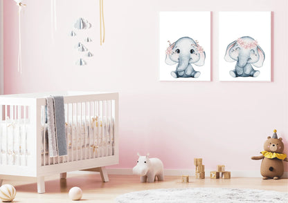 A modern, feminine nursery room featuring a white wooden crib set against a soft, dusty pink accent wall. Above the crib, two white-framed watercolor elephant prints are hung side-by-side. The soft grey elephants are detailed with delicate pink flower crowns, creating a harmonious and cohesive look against the warm pink background. The room includes a round woven jute rug and natural light, giving the space a modern, nature-themed, and soothing aesthetic.