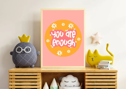 Decorative shelf with a 'You are enough' poster, plush toys, and books against a light wall.