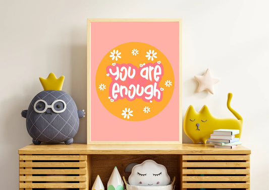 Decorative shelf with a 'You are enough' poster, plush toys, and books against a light wall.