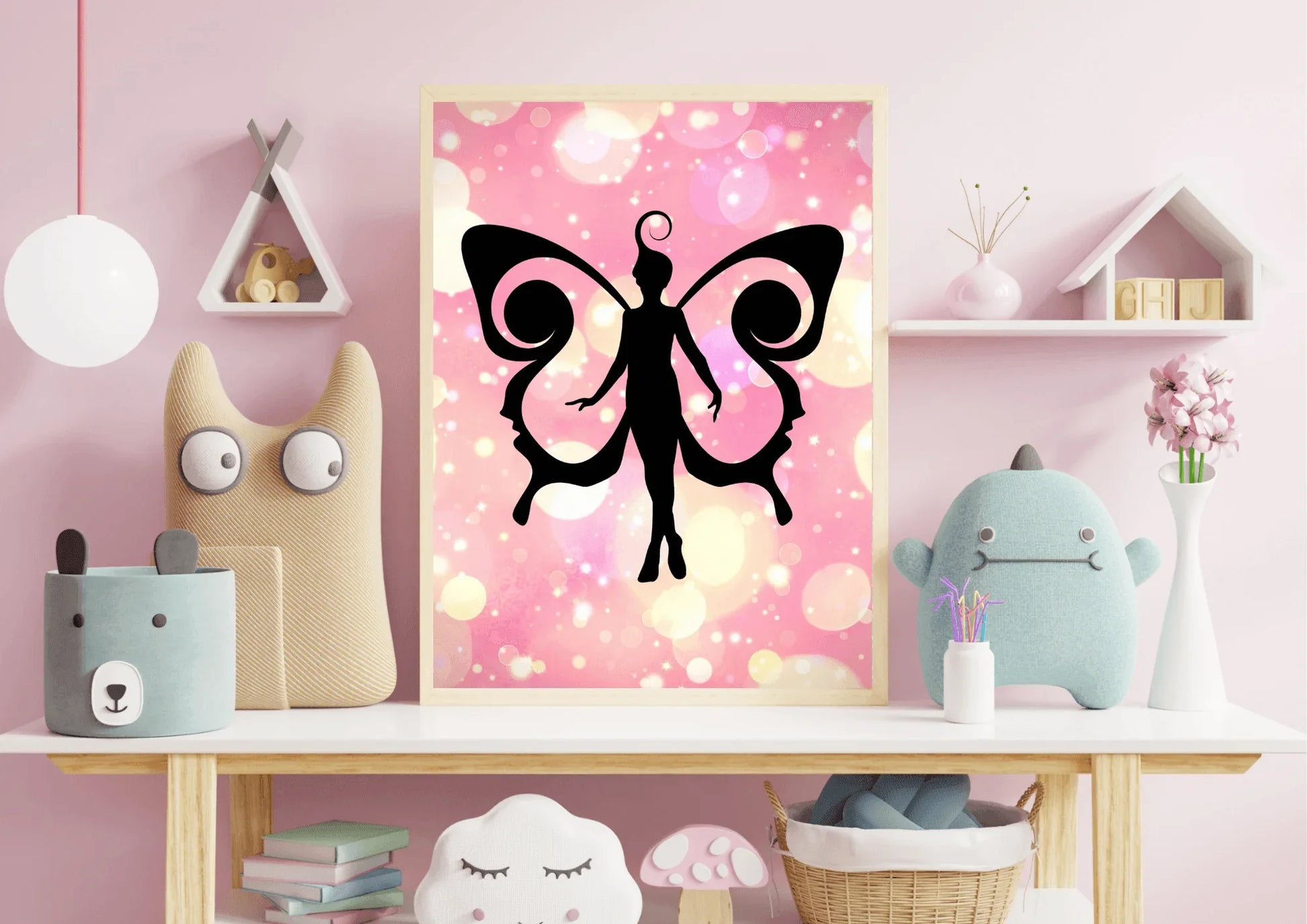 Framed fairy art print on a pink wall with decorative items below.