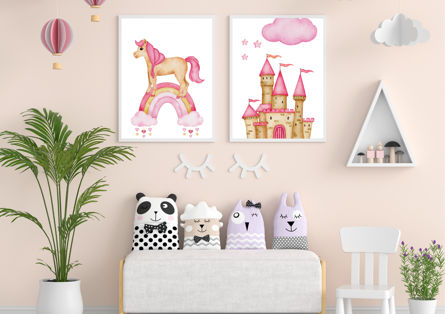 Two framed watercolor prints, one showing a unicorn on a rainbow and the other a pink princess castle, hang on a soft pink wall. Below the art, four animal-themed pillows rest on a white bench. To the left is a tall green houseplant, and to the right is a white triangular shelf with small wooden figures.