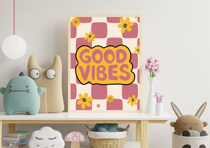 A framed art print with retro pink and yellow checkered squares and the words 'GOOD VIBES' in a yellow cloud shape, styled on a shelf in a cozy room setting with plush toys and flowers.