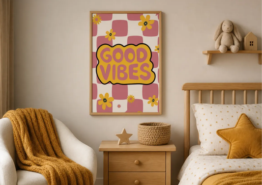 A framed wall art print with the words “GOOD VIBES” in yellow on a pink and cream checkered background, styled in a cozy children’s bedroom above a wooden nightstand and next to a bed.
