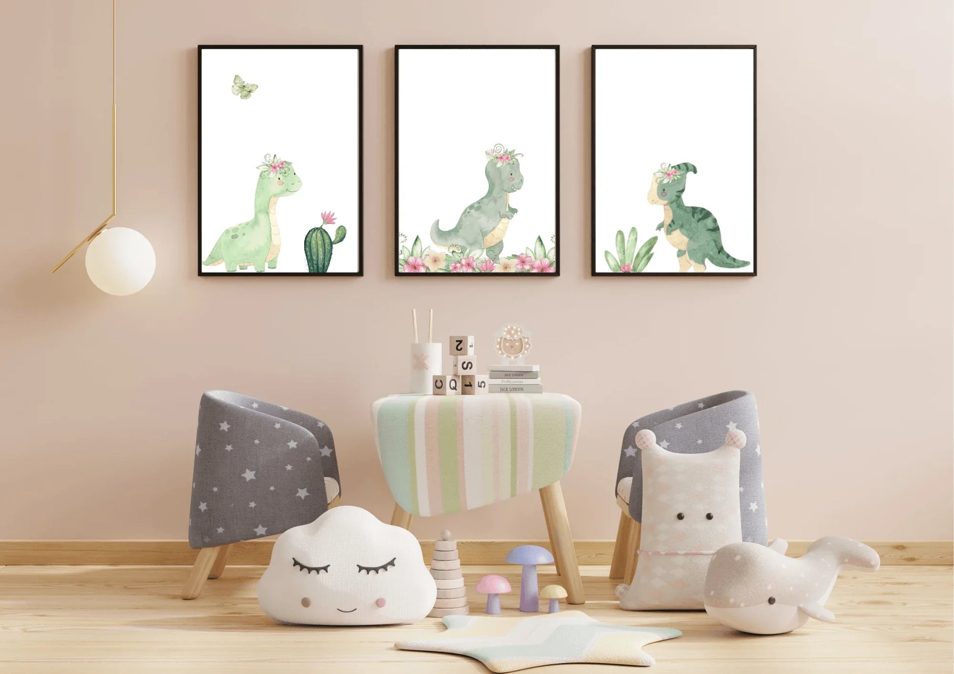 Nursery mockup showing three framed digital prints of cute, green watercolor dinosaurs wearing floral crowns. The artwork is hung on a pale pink wall above a low wooden table with small chairs.