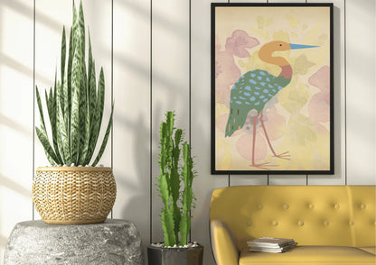 
A framed digital art print of a stylized heron, with a blue beak and a turquoise, spotted body, hanging on a white plank wall above a yellow couch. A large snake plant in a woven pot sits on a gray pedestal and a thin cactus stands next to it.