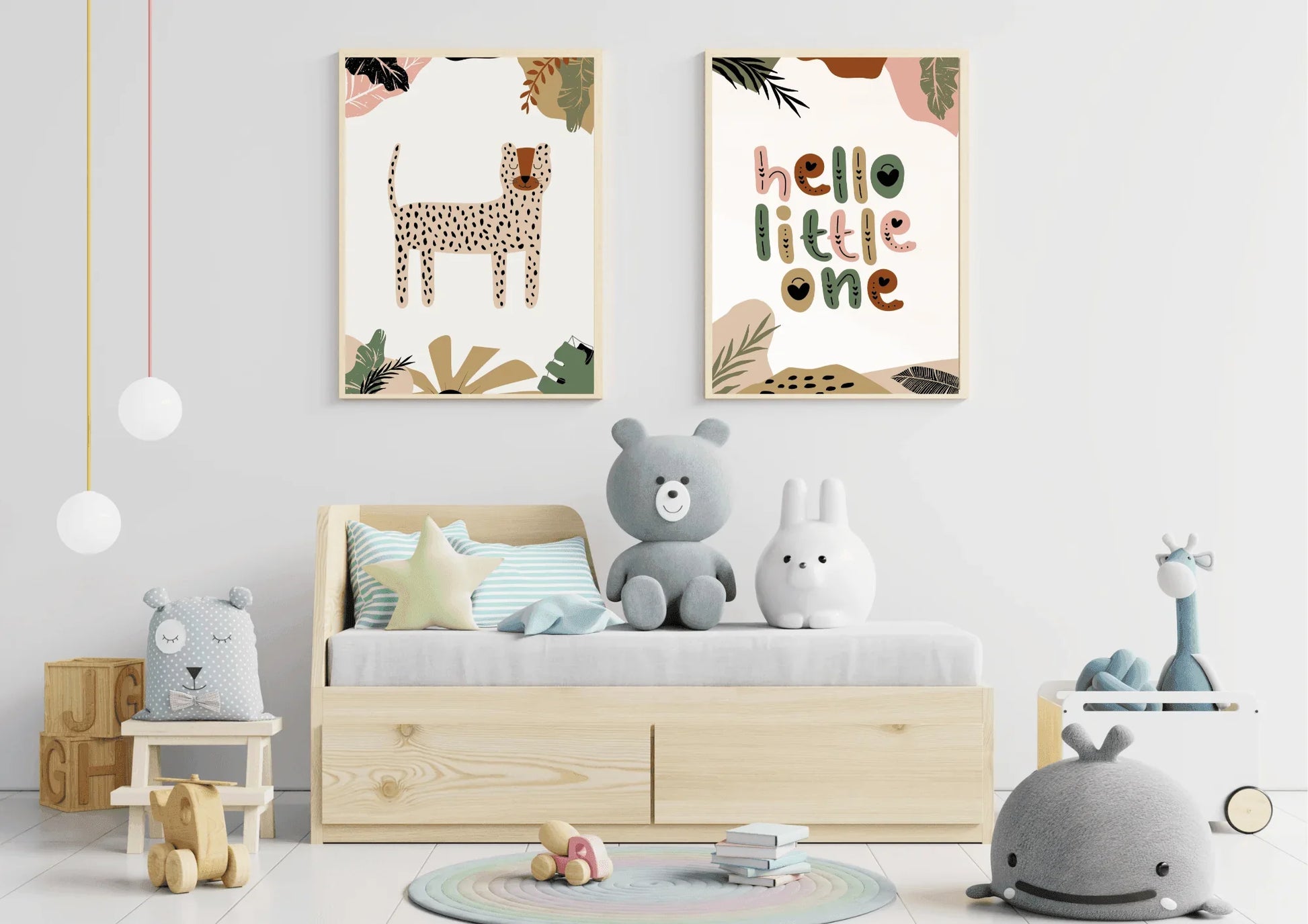 A child's room featuring a small wooden bed with storage drawers and several stuffed toys. A two-piece framed art set with a boho jungle theme, including a cheetah/leopard print and "hello little one," hangs above the bed.