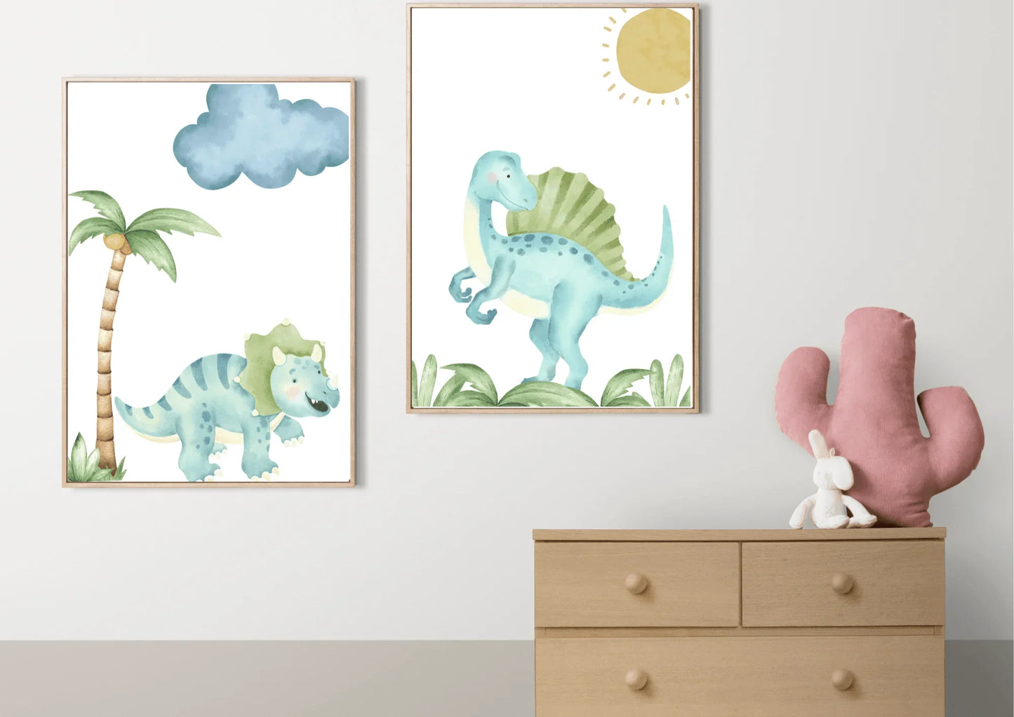 A set of two framed watercolor dinosaur art prints with wooden frames on a white wall above a dresser with a cactus pillow.