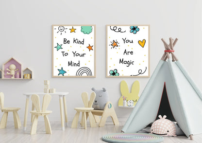 A two-panel set of framed digital art prints with motivational quotes, hanging on a white wall in a child's playroom. The left print says "Be Kind To Your Mind" and the right one says "You Are Magic." A small wooden table and chairs, a teepee, and various toys are in the room.
