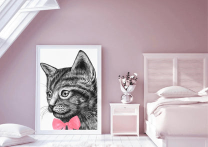 A framed digital art print of a black and white cat with a pink bow tie, leaning against a wall in a pink-walled bedroom with a bed and a white nightstand with a vase of flowers on it.