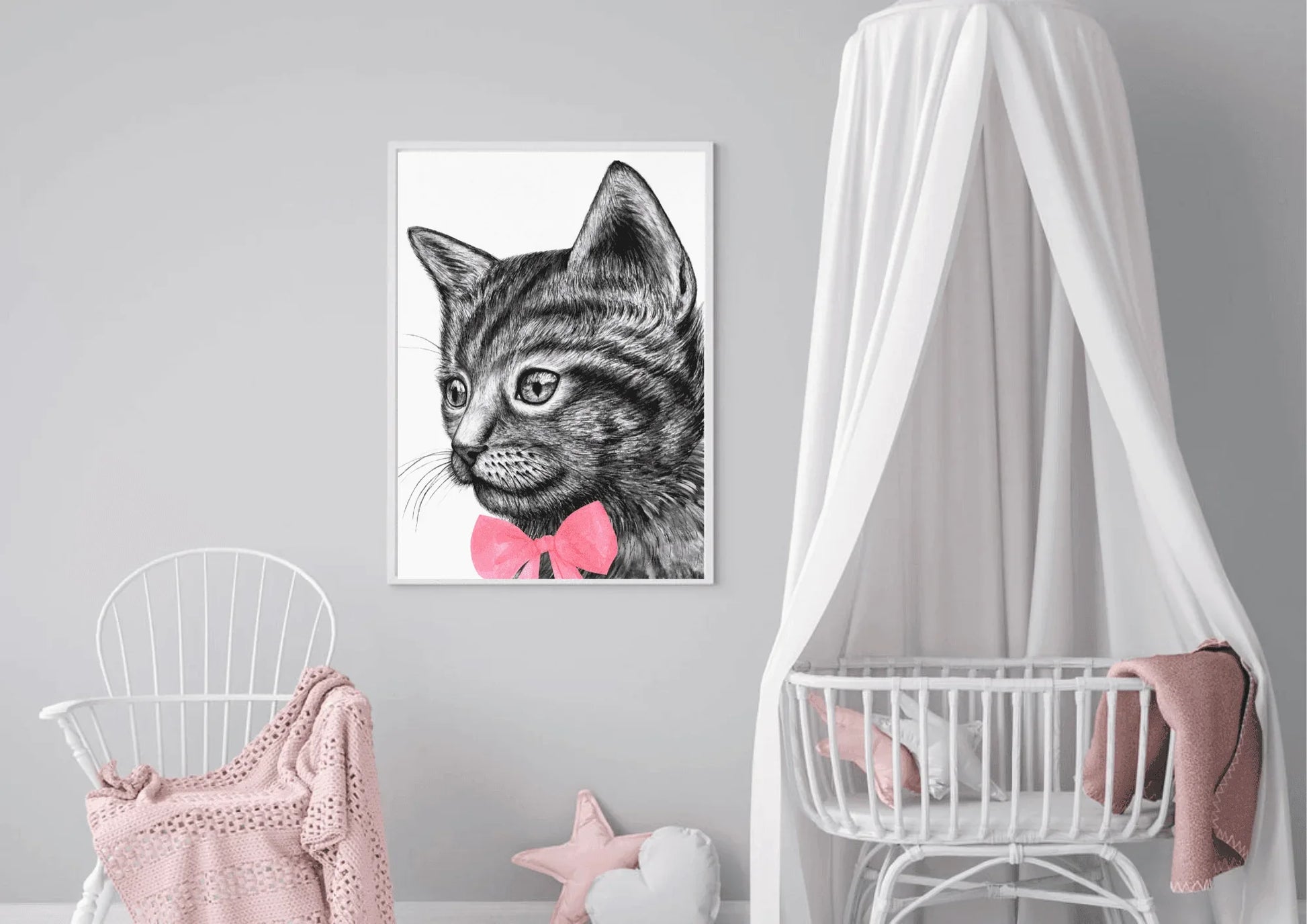 
A framed art print of a black and white cat with a pink bow tie hanging on a gray wall in a nursery. A white crib with a canopy and a white rocking chair with a pink blanket are in the room.