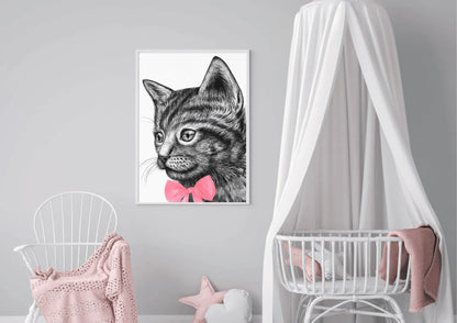 
A framed art print of a black and white cat with a pink bow tie hanging on a gray wall in a nursery. A white crib with a canopy and a white rocking chair with a pink blanket are in the room.