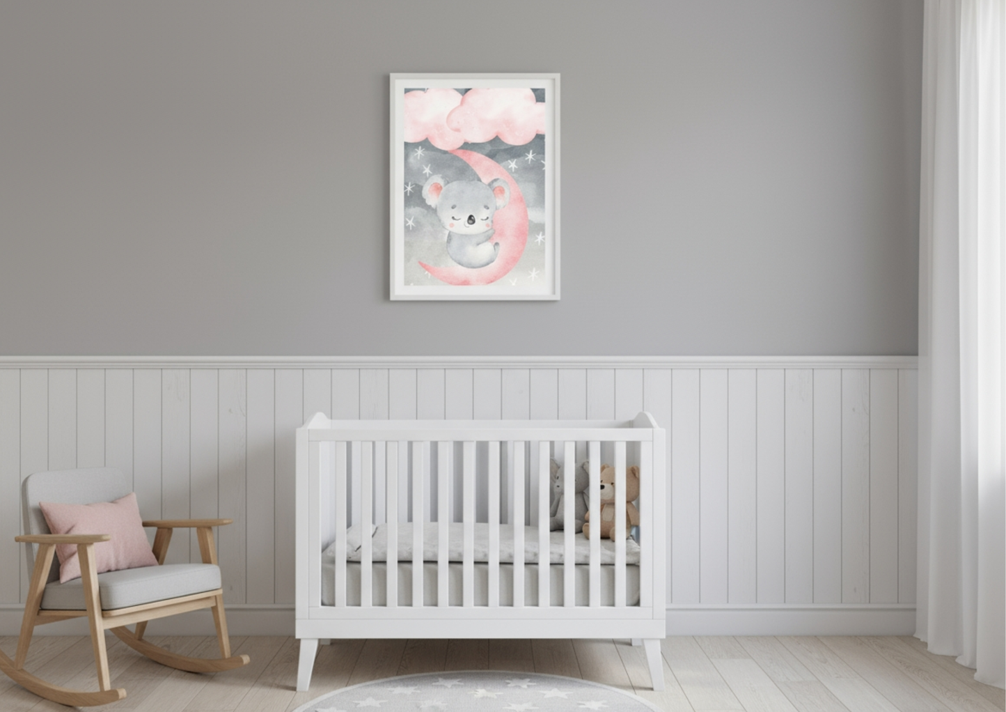 A simple and serene nursery room featuring light grey walls above a crisp white wainscoting or beadboard accent wall. Centered above a white wooden crib is a vertical framed watercolor print of a sweet, sleeping koala resting on a bright pink crescent moon, surrounded by grey clouds and scattered stars. To the left, a natural wood and grey upholstered rocking chair with a pink throw pillow adds a cozy element. The flooring is light wood, and the room is styled in a minimalist, gender-neutral grey and white 