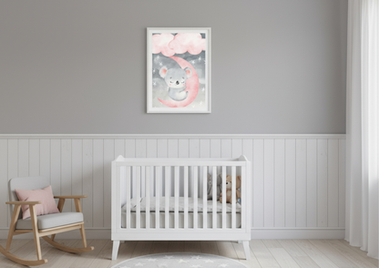 A simple and serene nursery room featuring light grey walls above a crisp white wainscoting or beadboard accent wall. Centered above a white wooden crib is a vertical framed watercolor print of a sweet, sleeping koala resting on a bright pink crescent moon, surrounded by grey clouds and scattered stars. To the left, a natural wood and grey upholstered rocking chair with a pink throw pillow adds a cozy element. The flooring is light wood, and the room is styled in a minimalist, gender-neutral grey and white 