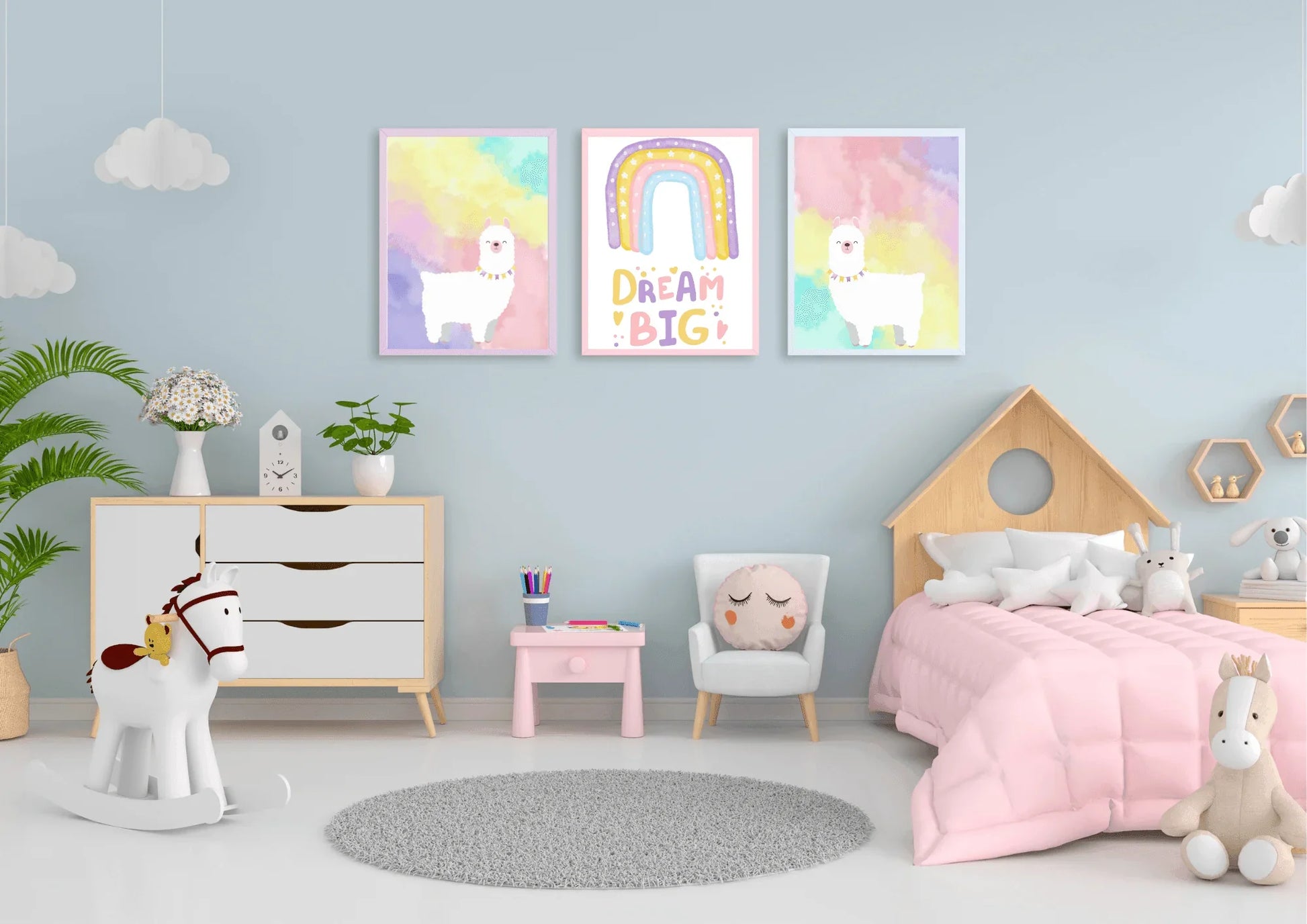 A set of three framed art prints with two llamas and a "Dream Big" quote on a light blue wall in a child's bedroom with a house-shaped bed.