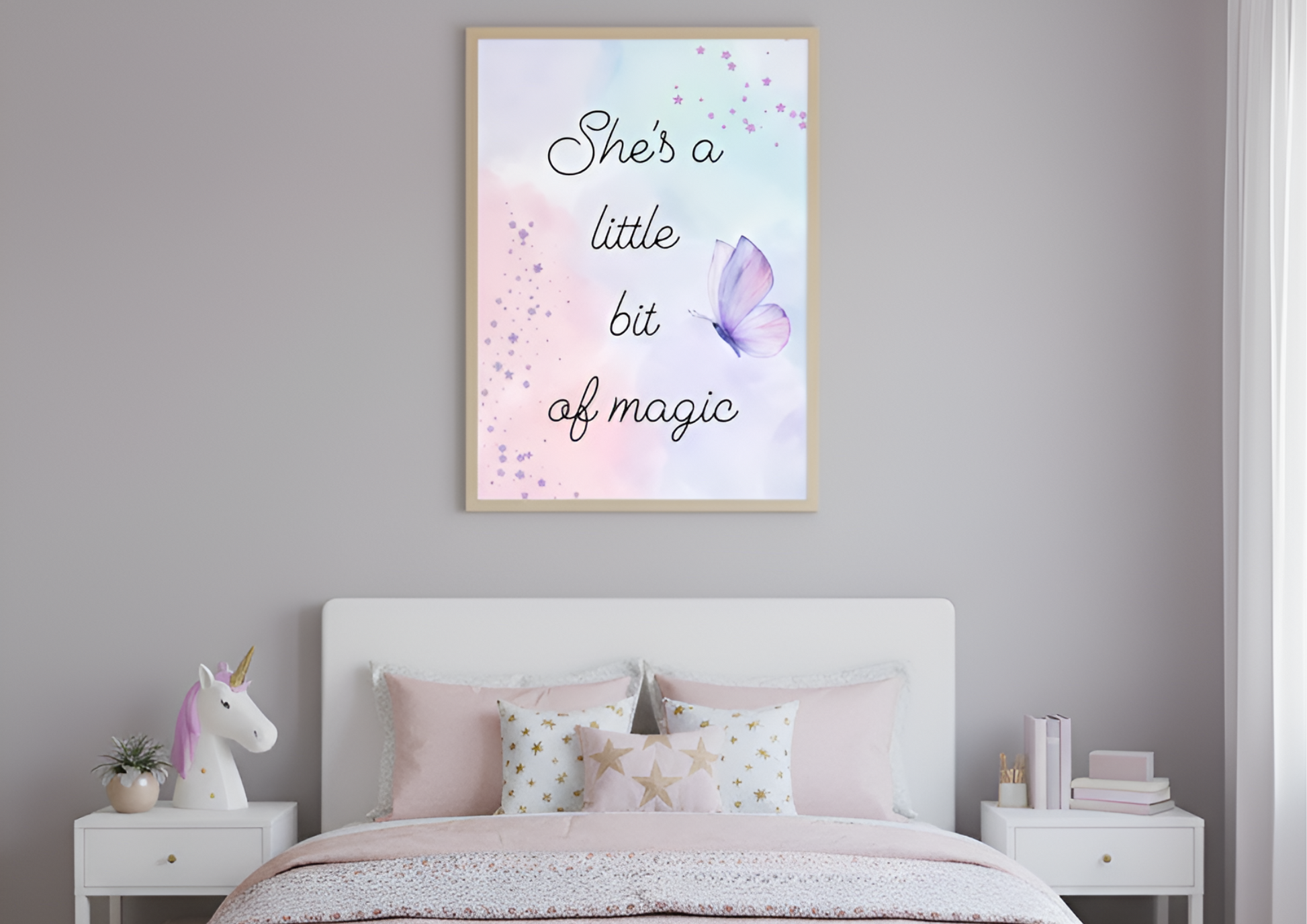 
A cozy girl's bedroom with light gray walls. A framed art print with a watercolor background and the phrase "She's a little bit of magic" hangs above a white bed. The bed is styled with light pink and gold star pillows, and there are two white nightstands on either side. One nightstand holds a unicorn lamp and a small plant, while the other holds a stack of books.
