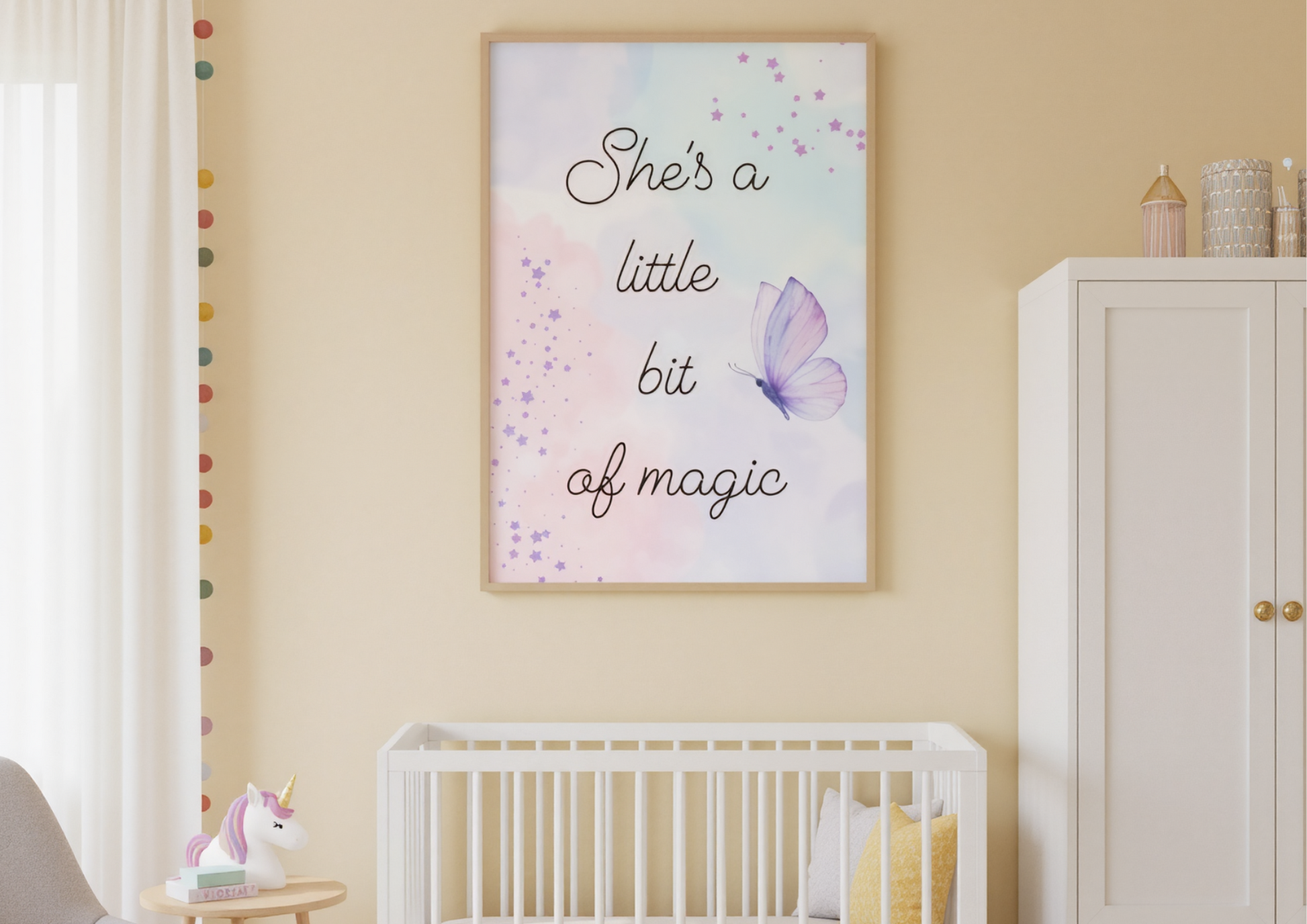 
A charming nursery with soft yellow walls. A framed art print with a watercolor background and the words "She's a little bit of magic" is hanging above a white crib with a light yellow pillow. A white wardrobe with gold handles is on the right, and a unicorn lamp is on a small table on the left.