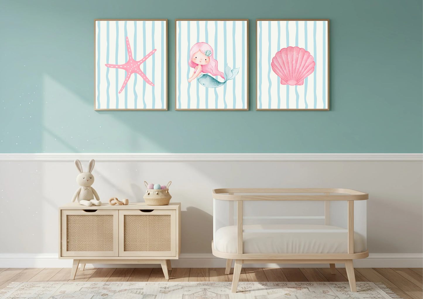 Three framed artworks of a mermaid, starfish, and shell on a wall above a crib and cabinet.