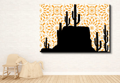 
A large canvas art print featuring a black silhouette of a desert landscape with saguaro cacti and a rocky mesa. The background is a bright orange mandala pattern with a white circular design. The print hangs on a white brick wall above a light wood rocking horse.
