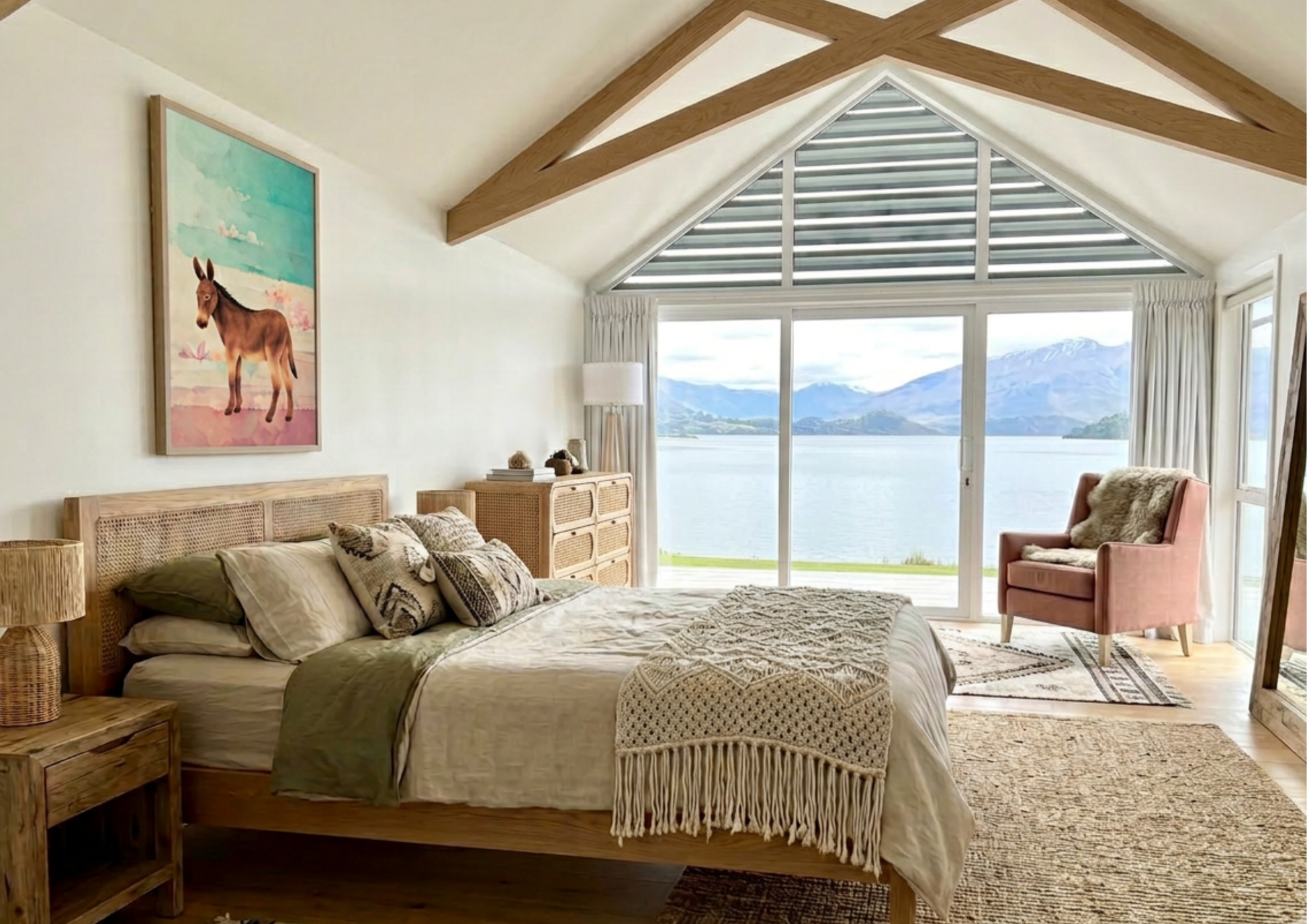 Bedroom with wooden bed, dresser, and large window view of a lake and mountains, and desert donkey wall art