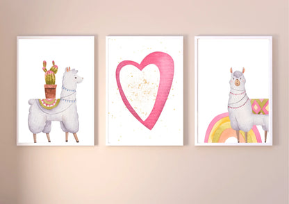 A set of three framed digital art prints featuring a llama with a cactus, a pink heart with gold speckles, and a llama standing on a rainbow. The prints are hanging in a horizontal line on a light tan wall.
