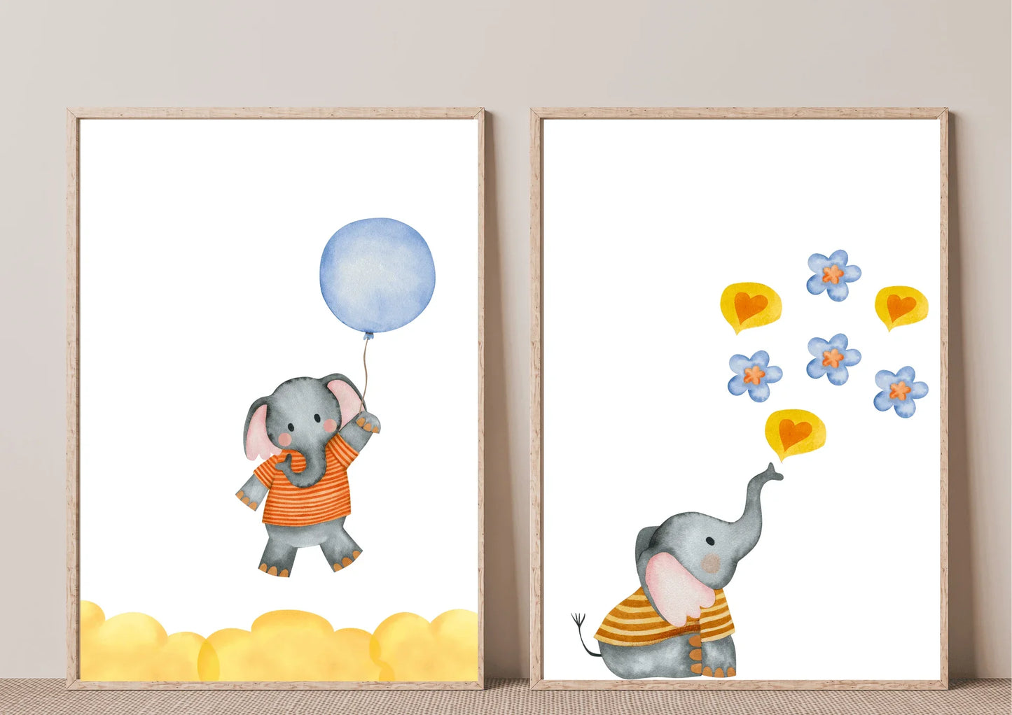 A close-up view of two framed watercolor elephant prints leaning against a white background. The print on the left shows an elephant in an orange striped shirt holding a blue balloon above yellow clouds. The print on the right shows an elephant in a yellow striped shirt blowing blue flowers and yellow hearts.