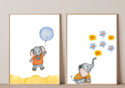 A close-up view of two framed watercolor elephant prints leaning against a white background. The print on the left shows an elephant in an orange striped shirt holding a blue balloon above yellow clouds. The print on the right shows an elephant in a yellow striped shirt blowing blue flowers and yellow hearts.