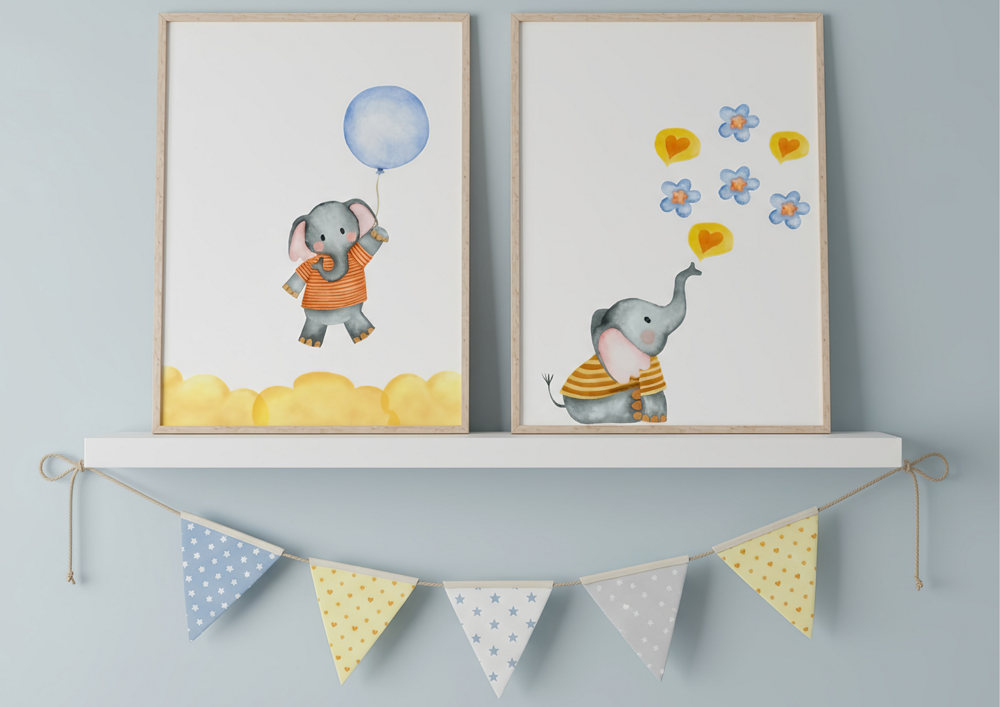 A close-up view of the two watercolor elephant prints hung on a light blue wall above a white shelf with a star-and-dot pennant banner strung beneath it. The prints feature an elephant with a blue balloon and an elephant blowing hearts and flowers.
