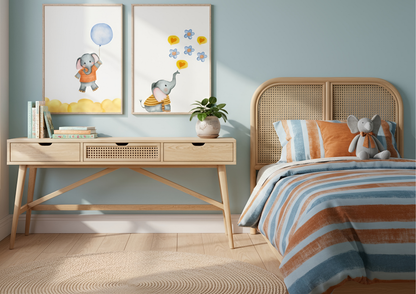 A child's bedroom with light blue walls and a rattan-style cane bed headboard. Two watercolor elephant prints are displayed above a wooden desk with cane drawers. The prints feature an elephant with a blue balloon and an elephant blowing hearts and flowers. The bedding is orange and blue striped, matching the colors of the prints.