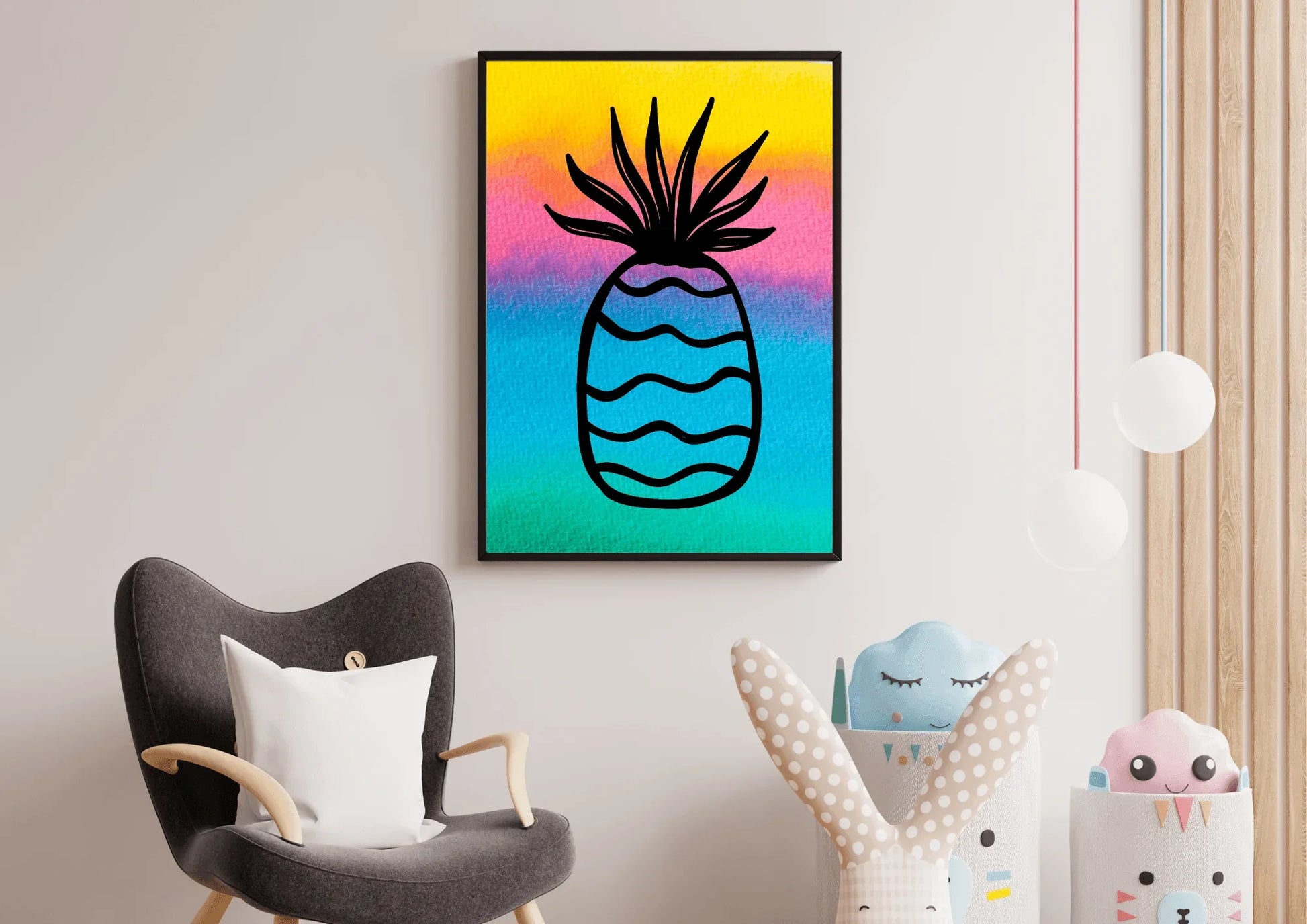 Framed watercolor pineapple print hanging on a pale wall in a nursery or playroom, positioned above a gray armchair and next to storage bins holding toys.