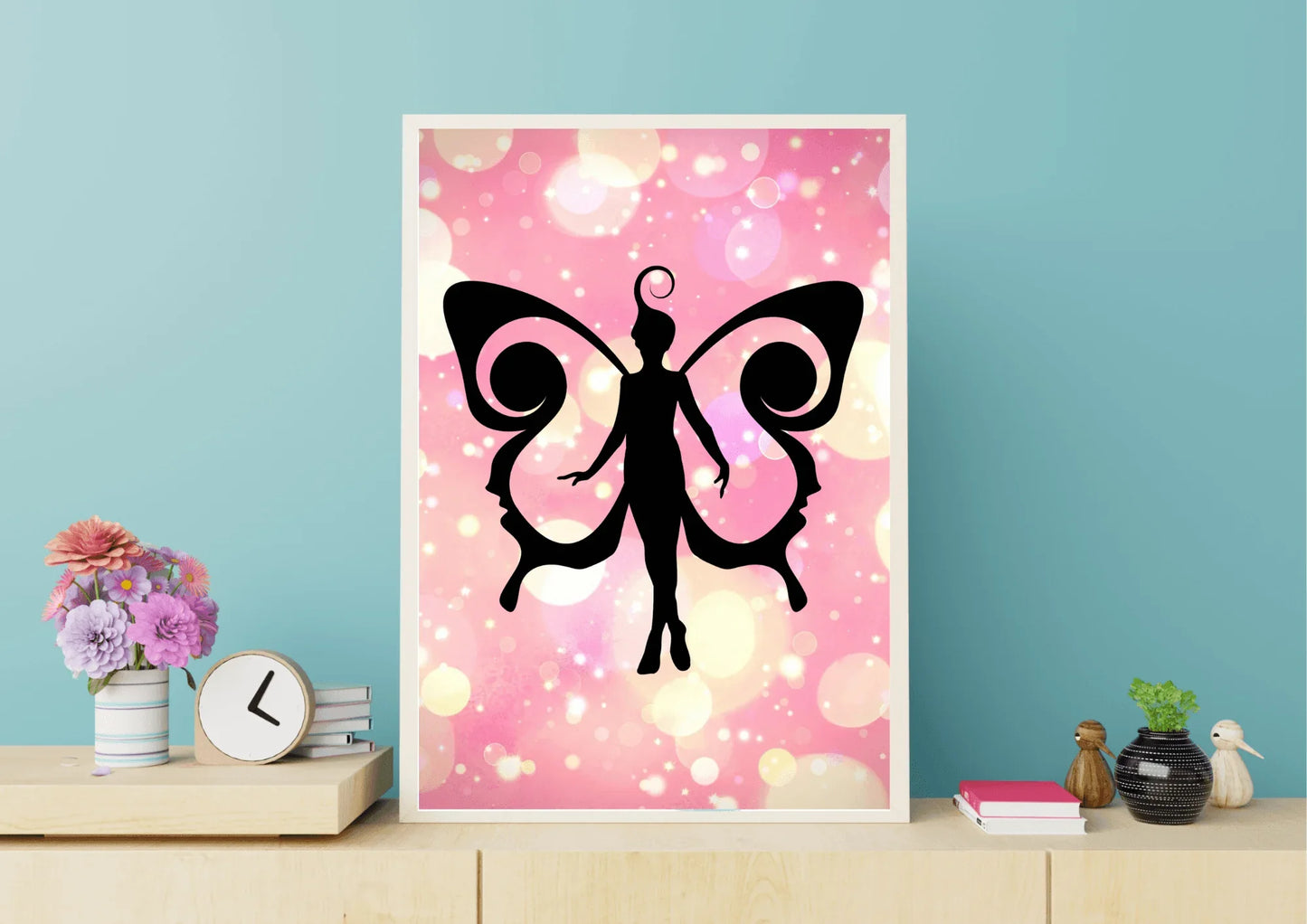 Framed artwork of a black fairy silhouette on a pink and white abstract background, displayed on a shelf.