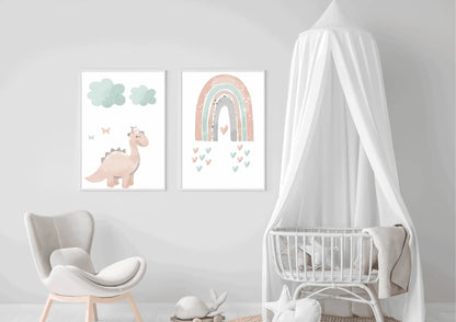 Two framed pastel prints (pink dinosaur with clouds, and a rainbow with hearts) on a white wall next to a baby crib with a canopy.