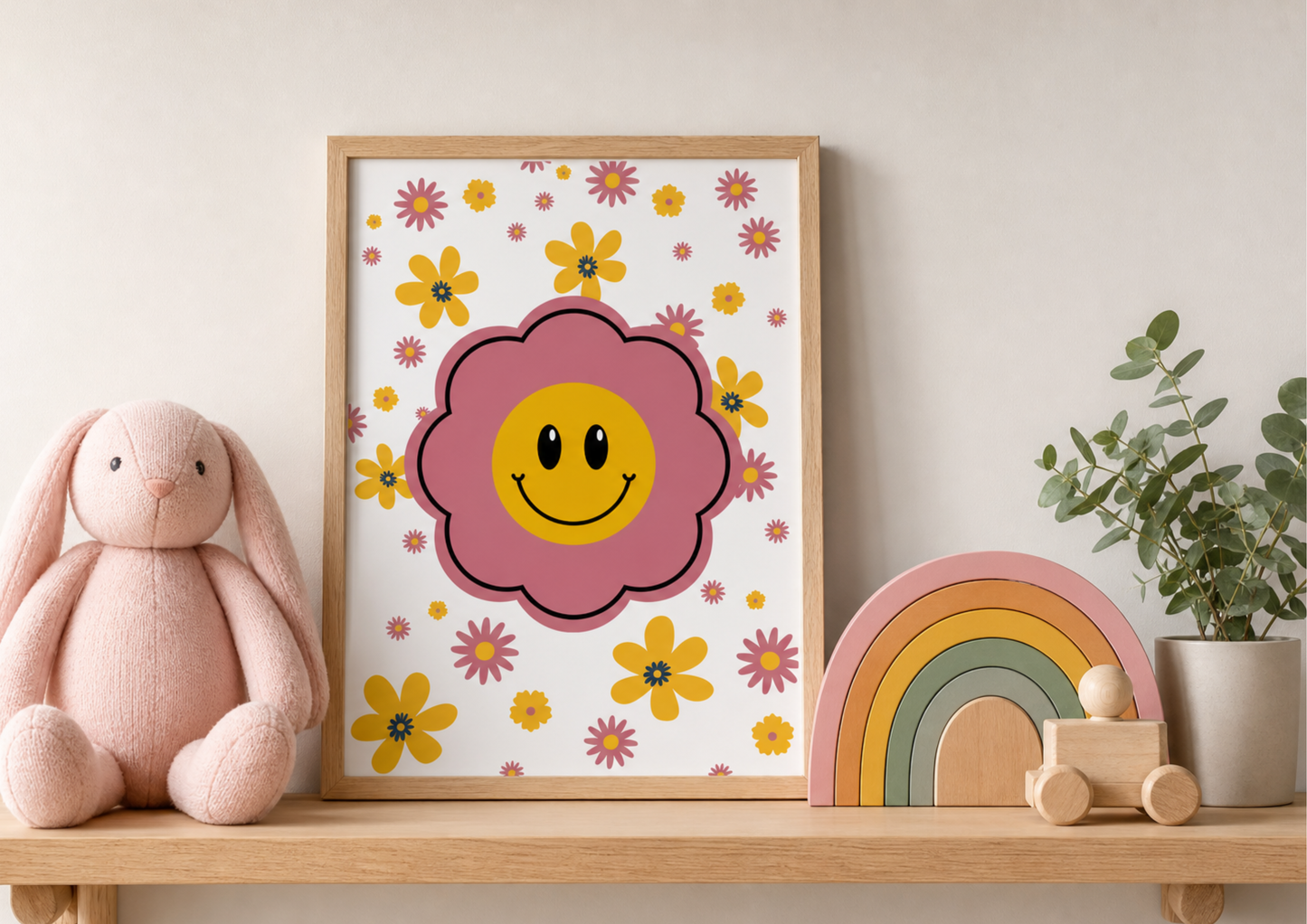 Framed retro-style nursery art print featuring a large pink flower with a yellow smiley face center, surrounded by smaller pink and yellow daisies, styled on a wooden shelf with a plush pink bunny, a wooden rainbow toy, and a small potted plant.