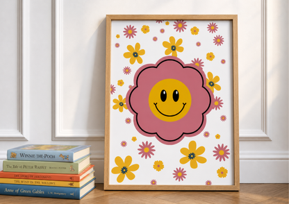 Framed retro-inspired nursery art print featuring a large pink flower with a yellow smiley face center, surrounded by smaller yellow and pink daisies, displayed next to a stack of classic children's storybooks including 'Winnie-the-Pooh' and 'The Tale of Peter Rabbit'.