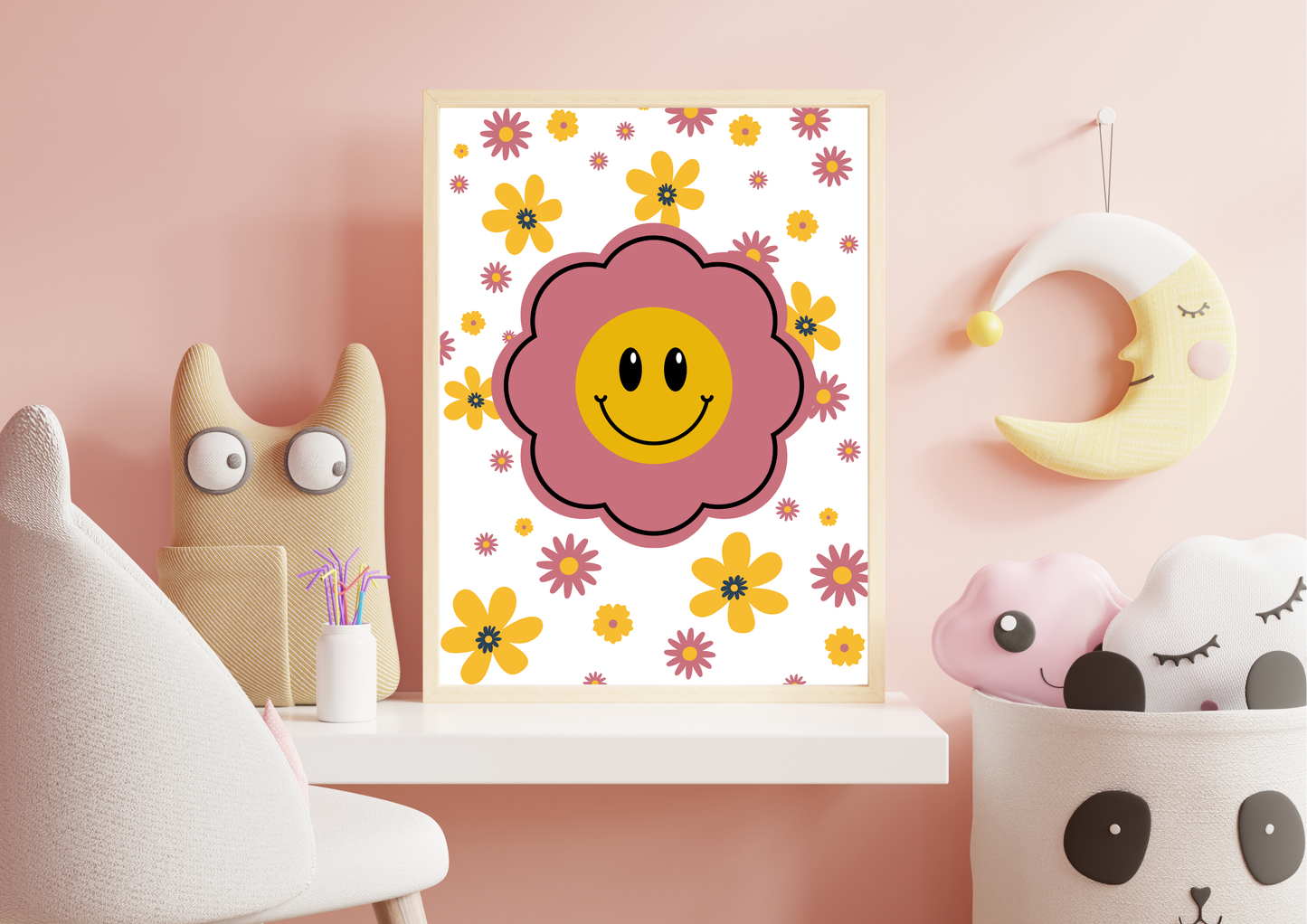 Framed retro-style nursery art print featuring a large pink flower with a yellow smiley face center, surrounded by smaller pink and yellow daisies, displayed on a shelf with whimsical decor including a crescent moon wall hanging, a plush monster toy, and a panda-themed storage basket.