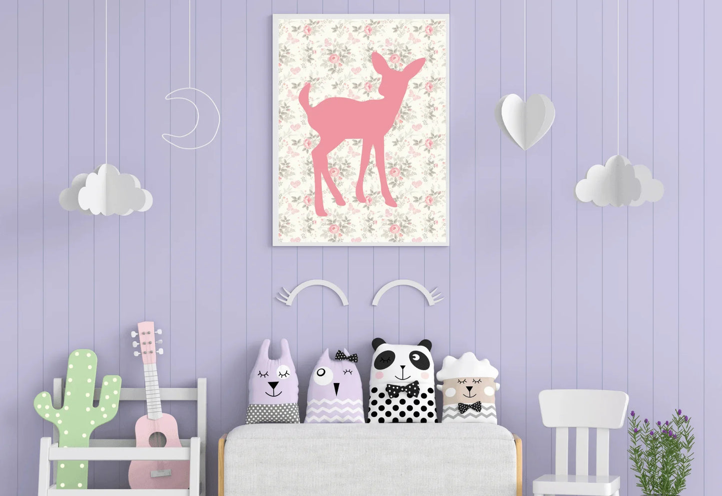 A framed digital art print of a pink deer silhouette on a floral background, hanging on a lavender-colored wall with white cloud and heart decorations. A sofa with four animal-themed pillows is placed below the print.