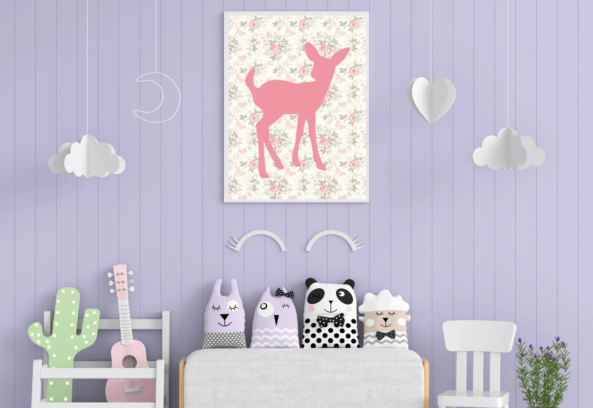 A framed digital art print of a pink deer silhouette on a floral background, hanging on a lavender-colored wall with white cloud and heart decorations. A sofa with four animal-themed pillows is placed below the print.
