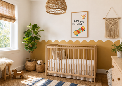 A styled nursery room featuring a light wood crib with white bedding, a yellow painted lower wall with a scalloped border, a framed 'Long live Boyhood' poster, a woven pendant light, and a potted fiddle-leaf fig plant.