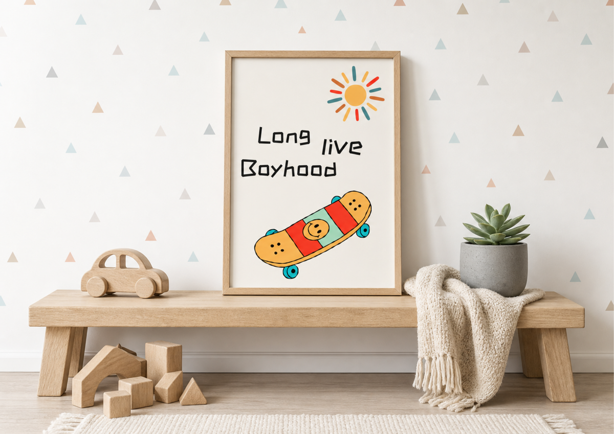 A framed art print with the text 'Long live Boyhood' and a colorful skateboard illustration, styled on a wooden bench in a nursery setting with a small plant and toy blocks.