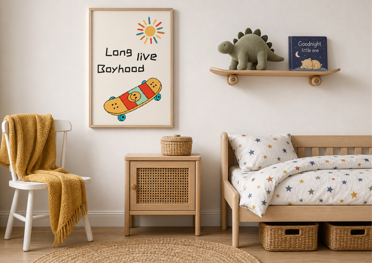 A styled children's bedroom corner featuring a framed art print with the text 'Long live Boyhood' and a colorful skateboard illustration. The room includes a wooden chair with a mustard yellow throw, a wooden side cabinet, a wooden bed with star-patterned bedding, and a shelf with a green dinosaur toy and a book.