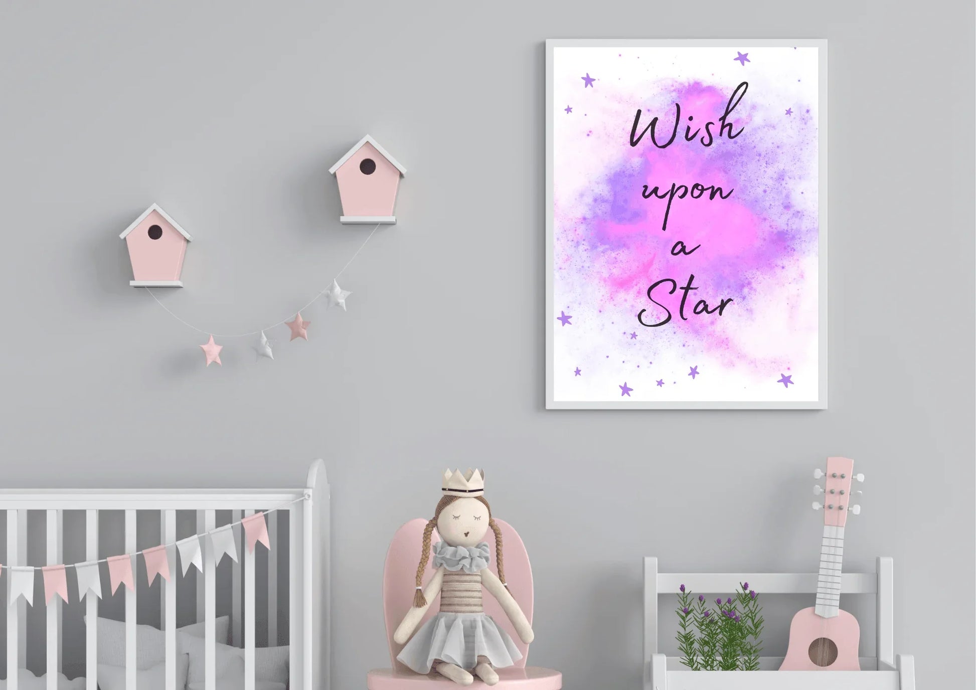 A framed "Wish upon a Star" nursery print with a purple and pink watercolor galaxy, hanging on a gray wall above a white crib, a stuffed doll, and a pink toy guitar.