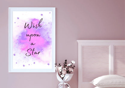 A framed "Wish upon a Star" nursery print with a purple and pink watercolor galaxy, hanging on a light pink wall above a white bed and a bouquet of flowers.