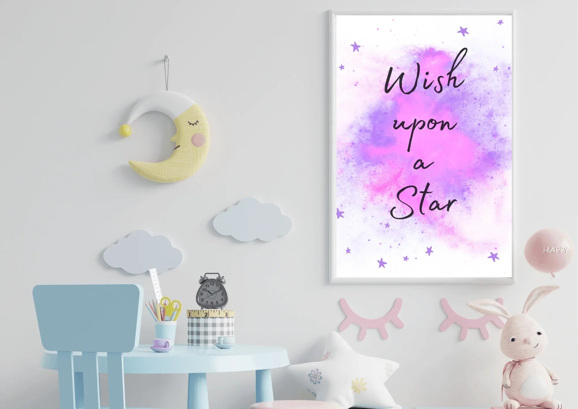 A framed "Wish upon a Star" nursery print with a purple and pink watercolor galaxy, hanging on a white wall above a small blue table with a clock and stationery.