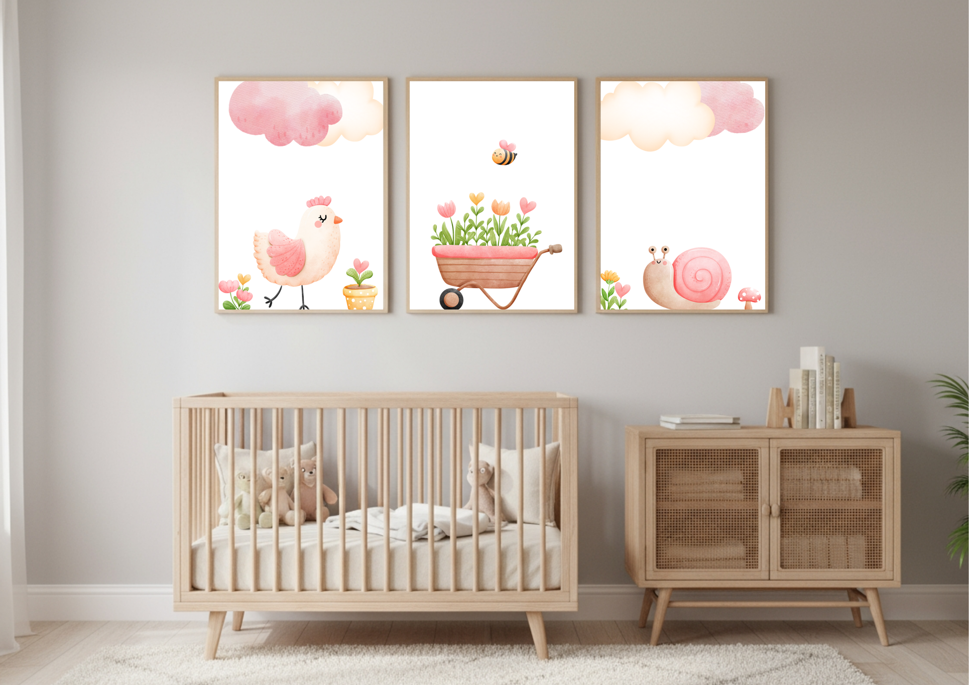 A close-up view of the set of three Farm Nursery prints displayed above a natural wood crib and a low wooden storage cabinet with cane webbing doors. The wall is light gray, and the prints feature a pink chick, a wheelbarrow of flowers with a bee, and a pink snail, all beneath pink clouds.