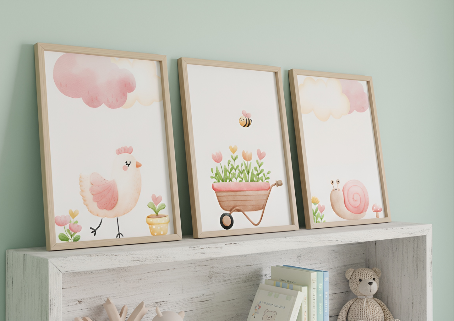 A close-up view of the three watercolor Farm Nursery prints leaning on a distressed white wooden shelf against a mint green wall. The prints feature a pink chick, a wheelbarrow of flowers with a bee, and a pink snail. The shelf below holds books and a soft, crocheted teddy bear.