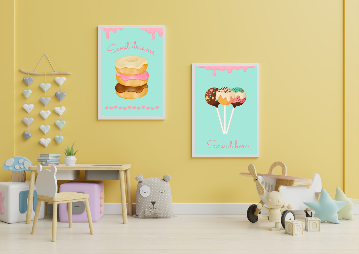 A set of two framed art prints of donuts and cake pops on a yellow wall in a child's playroom.
