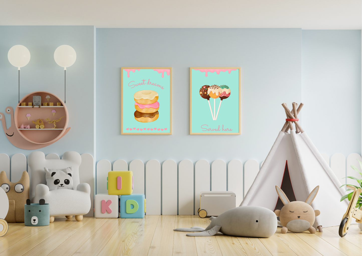 A set of two framed art prints of donuts and cake pops on a light blue wall in a child's playroom with a teepee and toys.