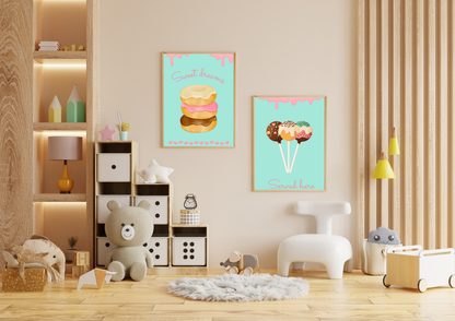 A set of two framed art prints of donuts and cake pops on a beige wall in a child's playroom with a bookshelf and a teddy bear.