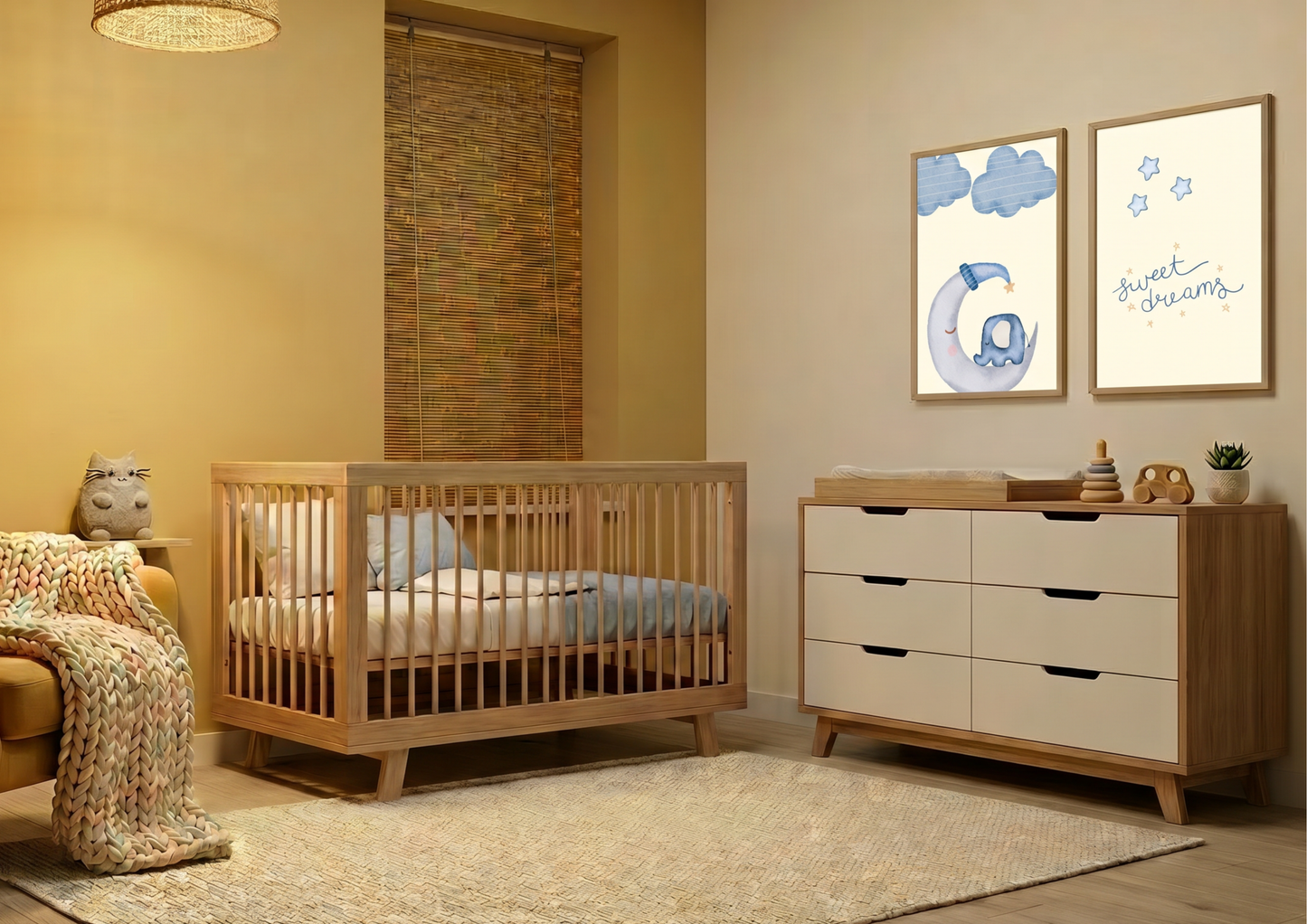 A warm and inviting Scandinavian-style nursery featuring a mustard-yellow accent wall and light-wood furniture. In the center, a natural wood crib sits on a large cream textured rug, with a thick, colorful chunky-knit blanket draped over a chair in the foreground. To the right, a wooden dresser with white drawer fronts serves as a changing station, topped with wooden toys and a small plant. Above the dresser, two wooden-framed prints are displayed: one of a whimsical elephant on a crescent moon and another 