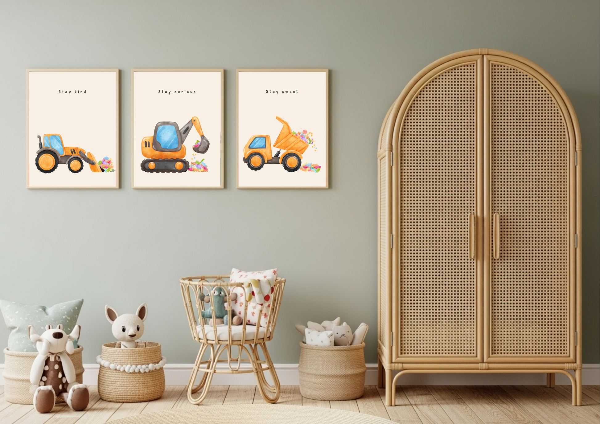 Set of three framed watercolor construction vehicle prints (Stay Kind, Stay Curious, Stay Sweet) hanging on a sage green nursery wall above a natural rattan crib and cabinet.